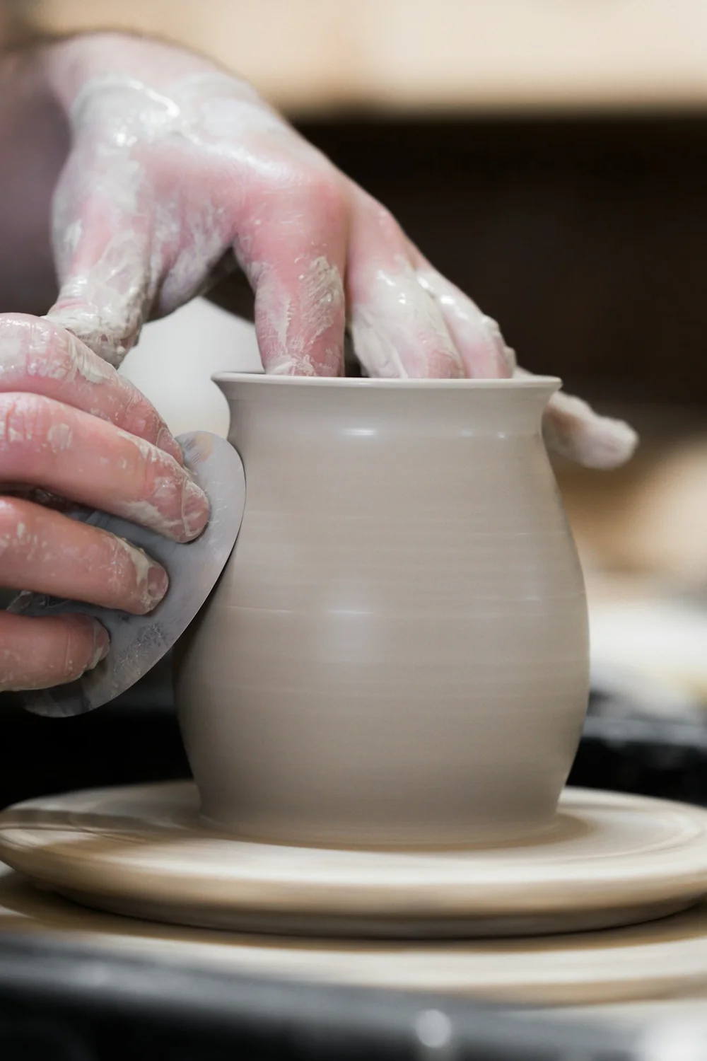 Hands shaping a clay pot on a pottery wheel
